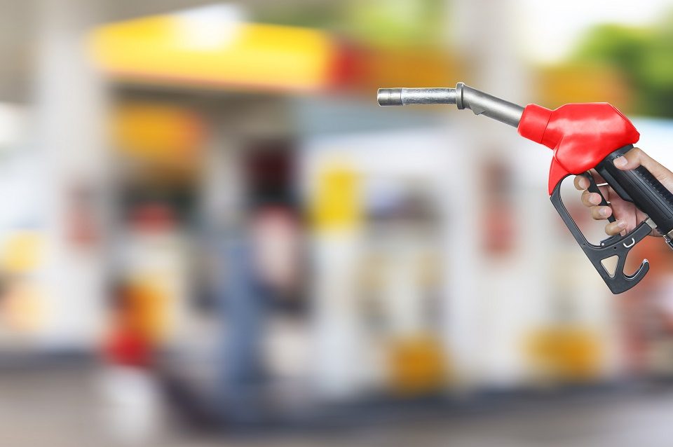 Man In Suit Holding A Fuel Nozzle In Front Of A Gas Station