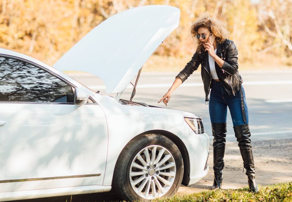 blonde woman on the side of the road with a broken car